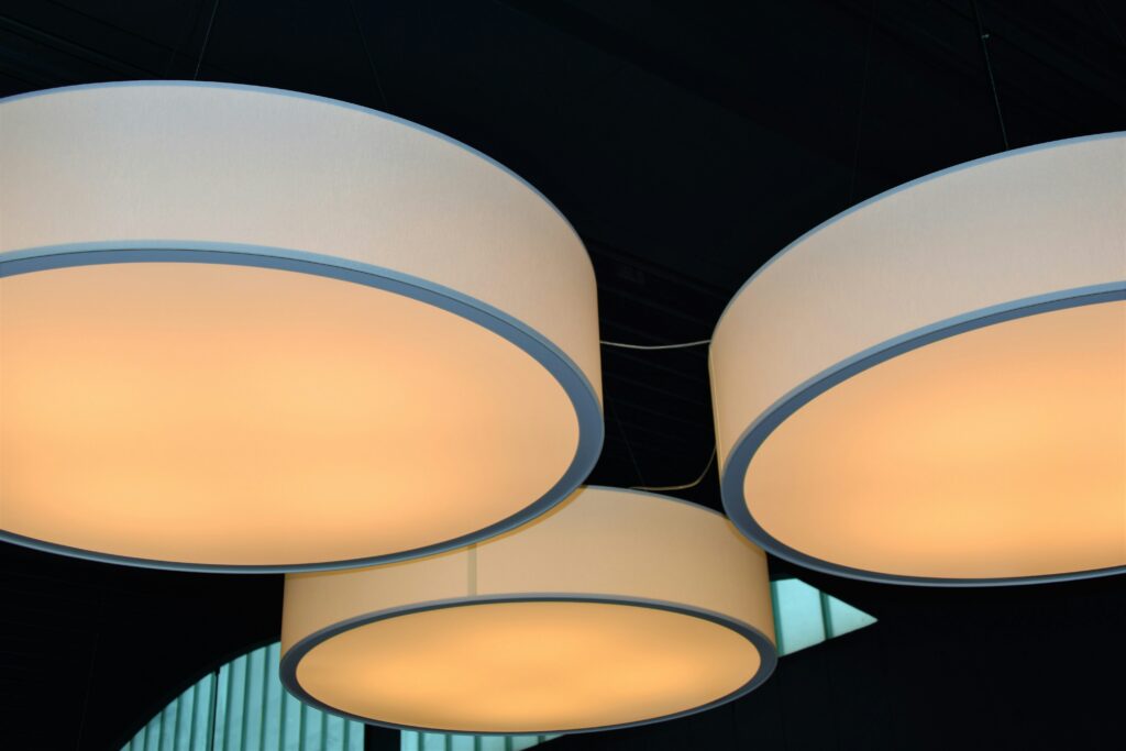 Trzy duże, nowoczesne lampy sufitowe o ciepłym świetle, zawieszone w eleganckim wnętrzu restauracji.